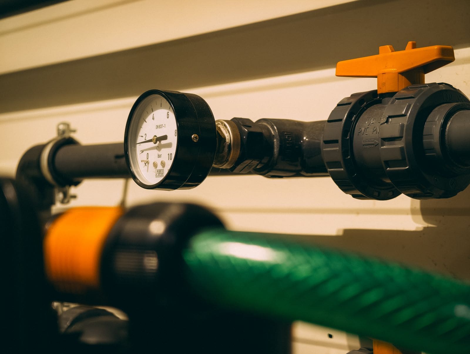 Close-up of a pressure gauge, valve and pipework with an orange-handled valve and a hose