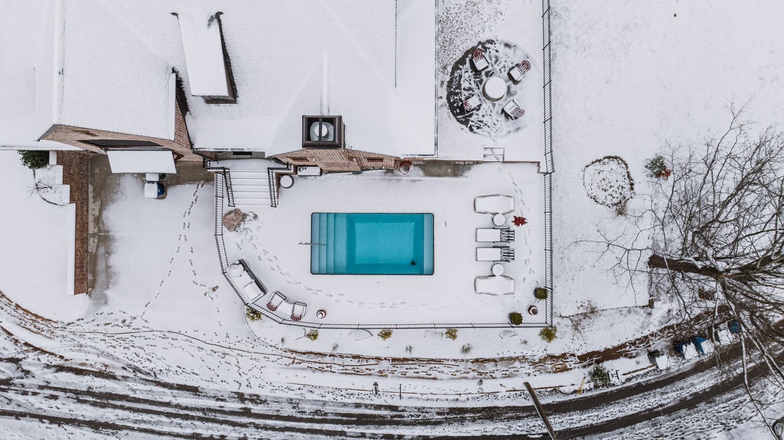 Aerial view of a snow-covered house with a backyard pool and patio seating