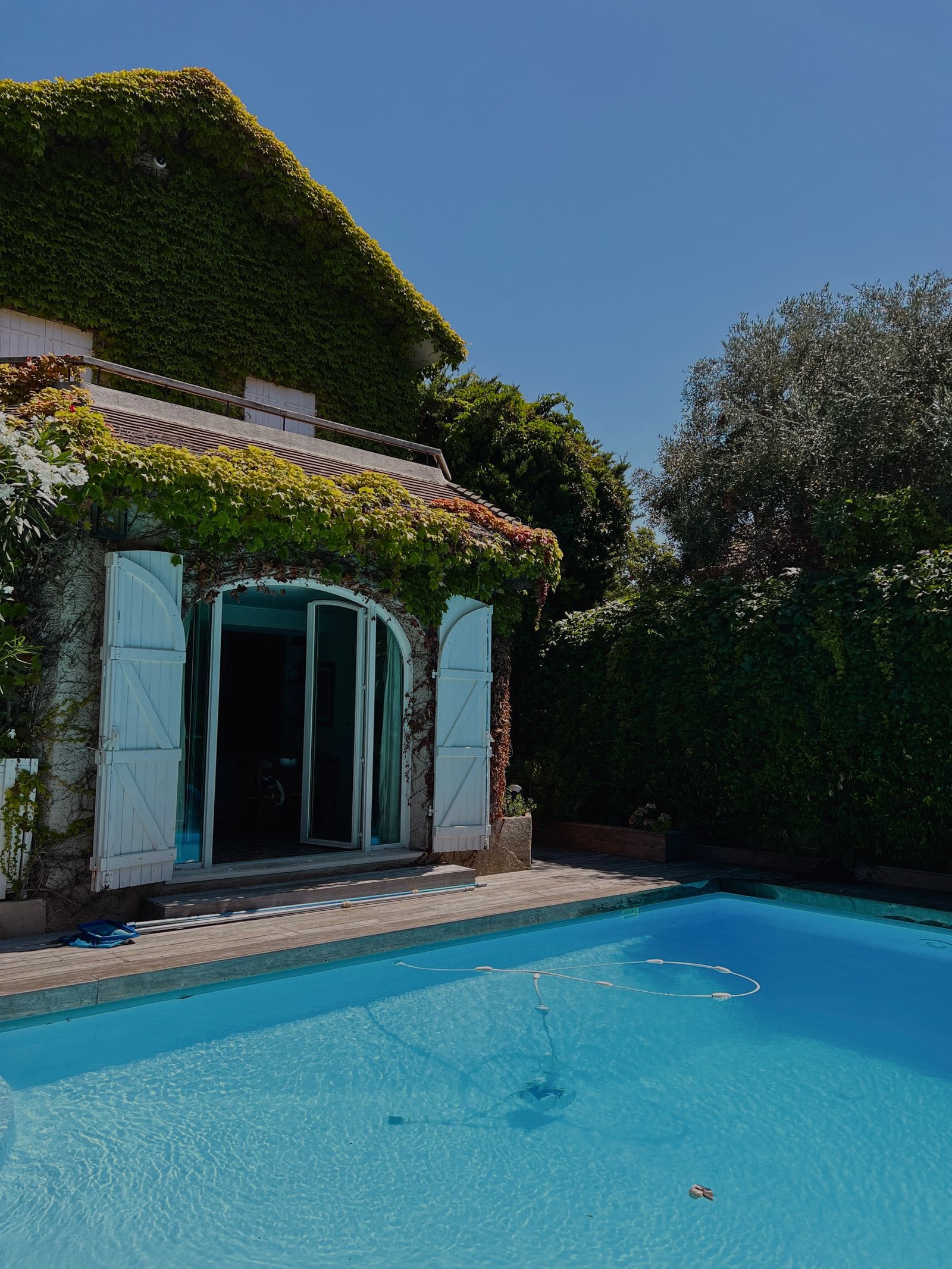 A backyard pool beside a house with an automatic pool cleaner hose floating on the surface