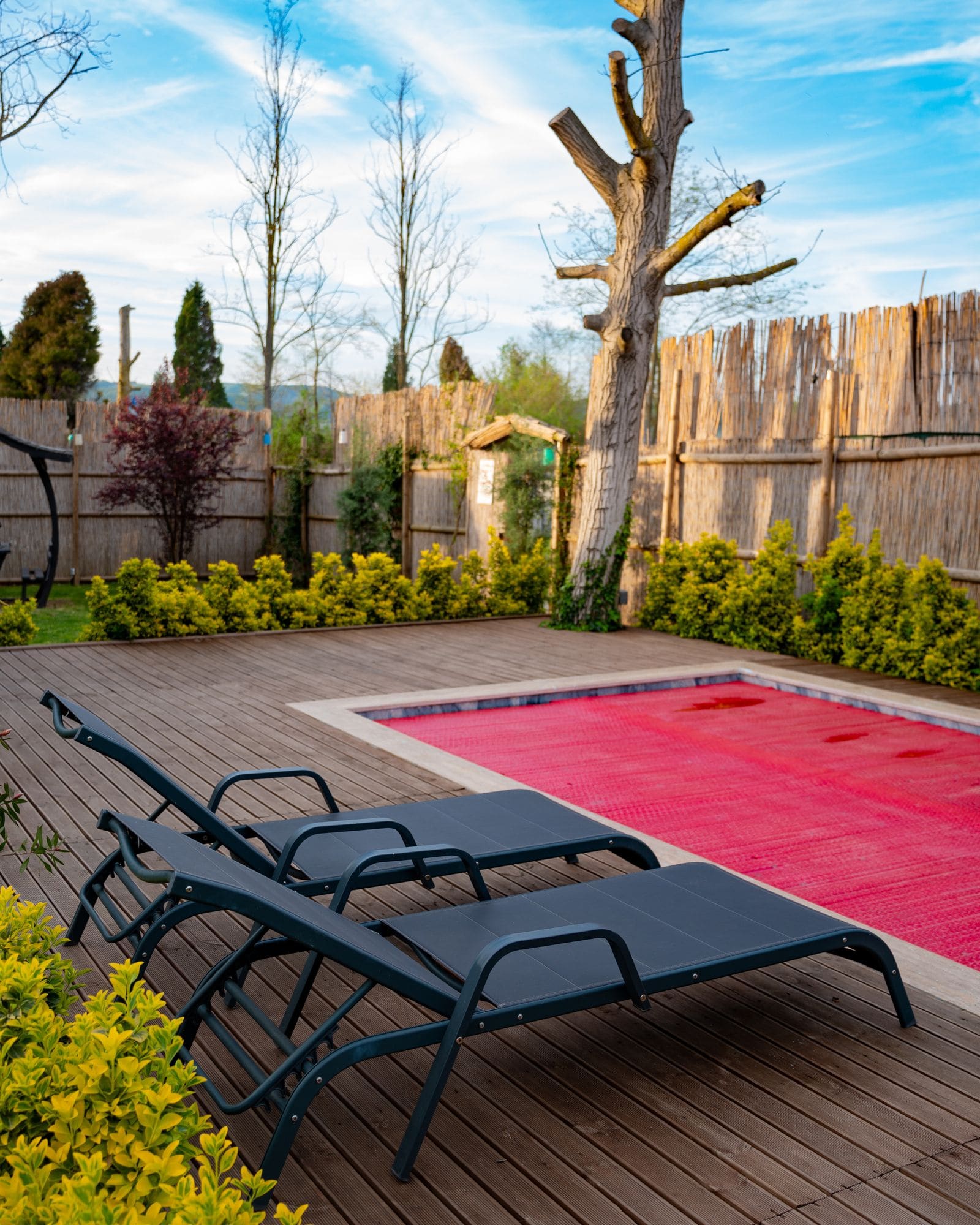 A pool with a red cover over the water, wooden deck and two lounge chairs